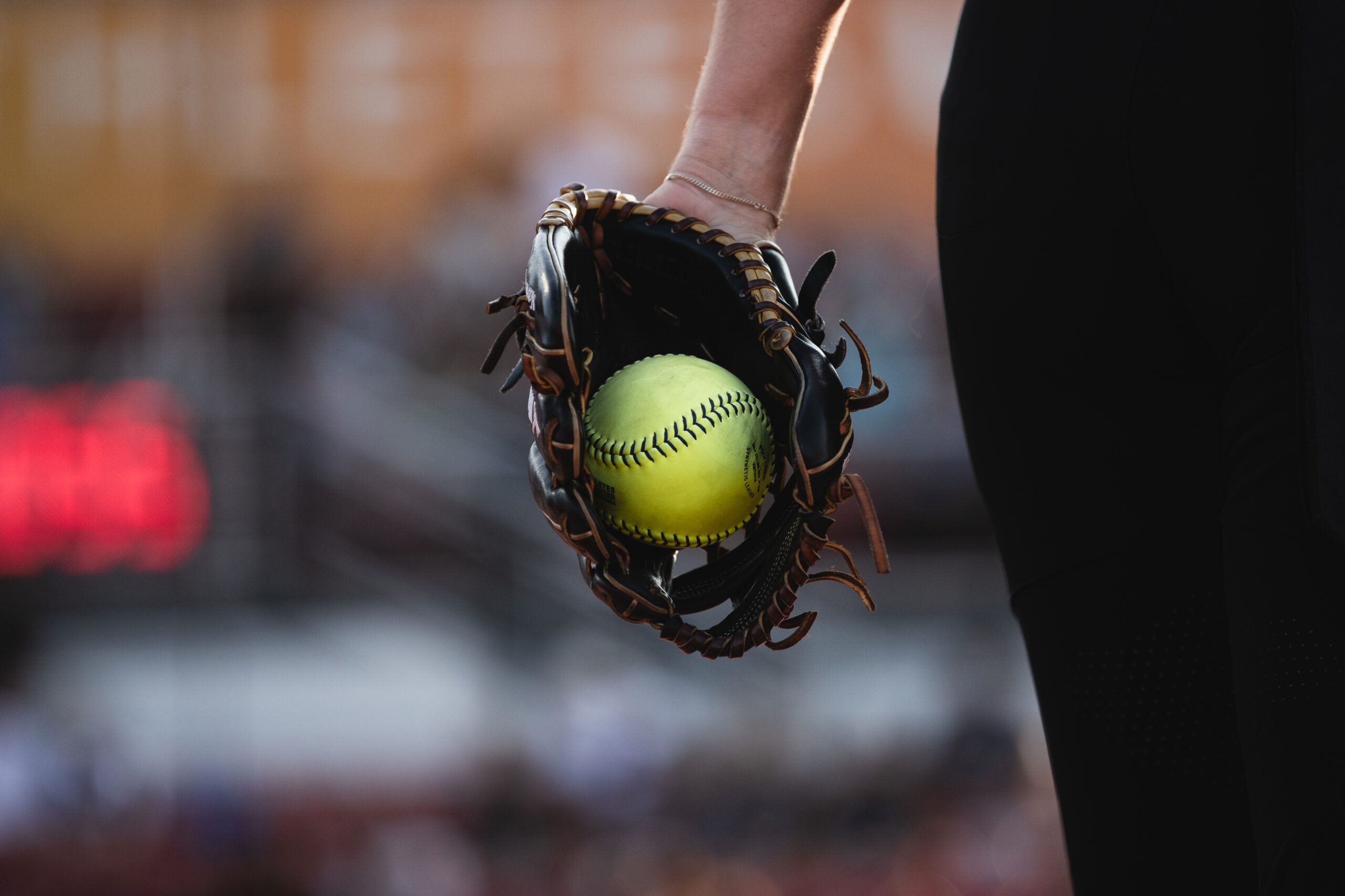 Softball player holding a glove at her side with the ball visible in the pocket.